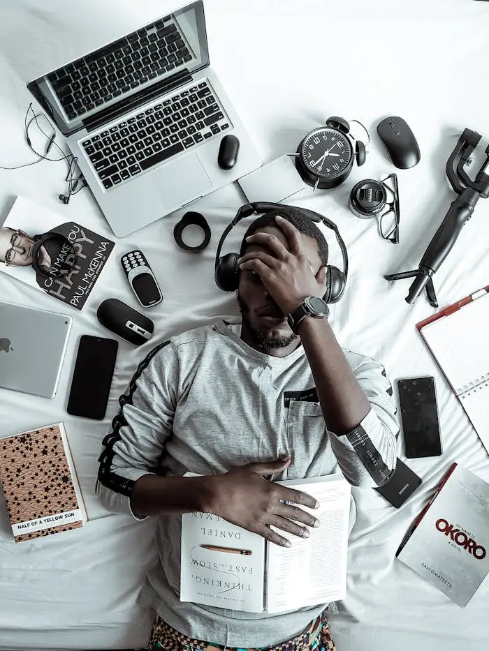 Home A young man lying on a bed surrounded by modern gadgets, books, and tech devices, illustrating digital lifestyle.