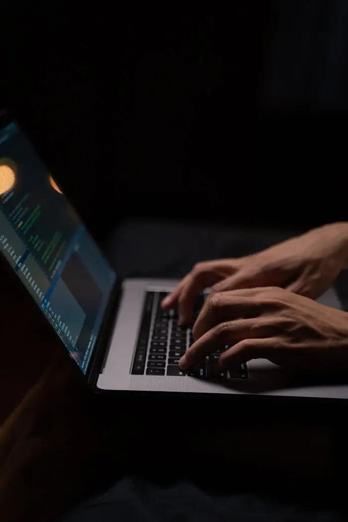 Home Hands typing code on a laptop keyboard in a dark room, capturing the essence of late-night programming.